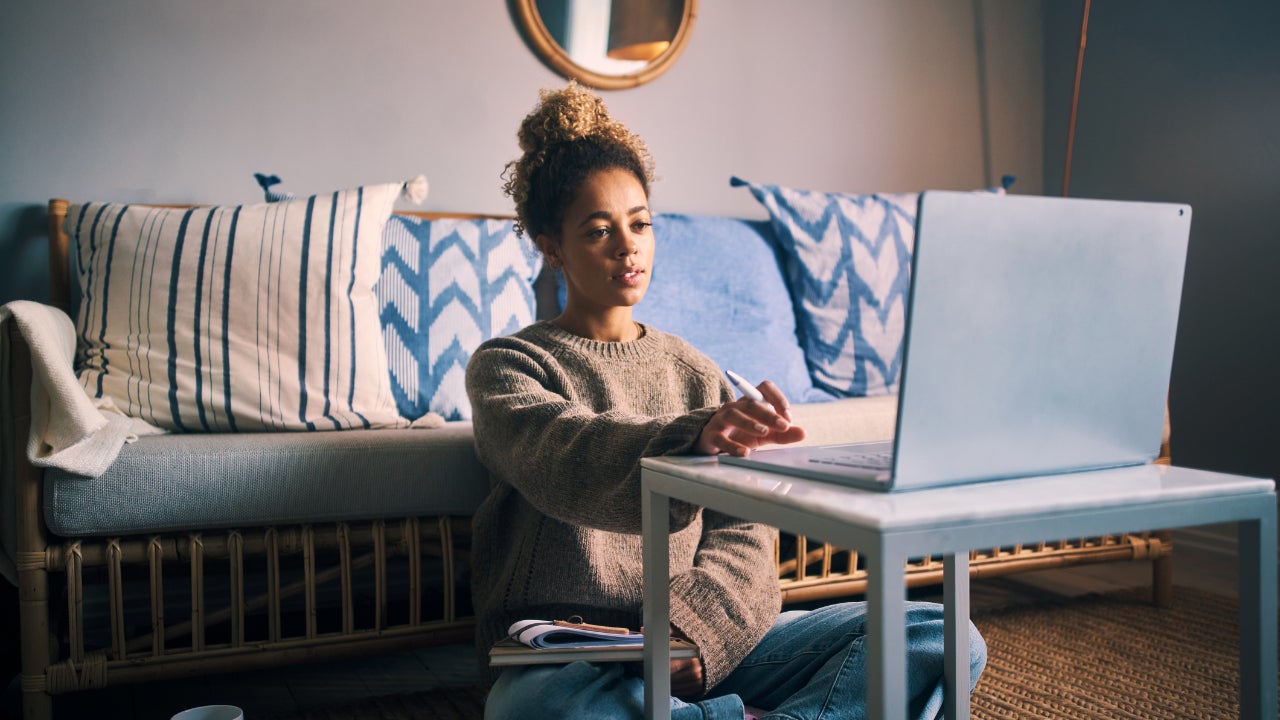A freelancer sits on the floor in her living room, looking at her laptop.