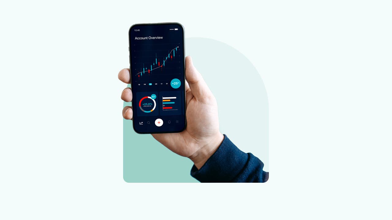 A hand holds up a phone with a stock chart on the screen.