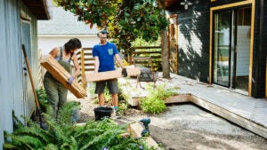 A couple carries lumber to build garden beds in the backyard.